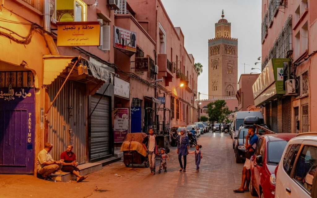 The Koutoubia minaret rising over a rose-pink medina street in Marrakech at dusk